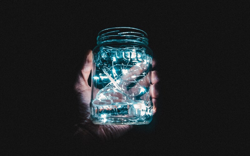 A hand holding a mason jar full of blue battery-powered string lights in the dark.