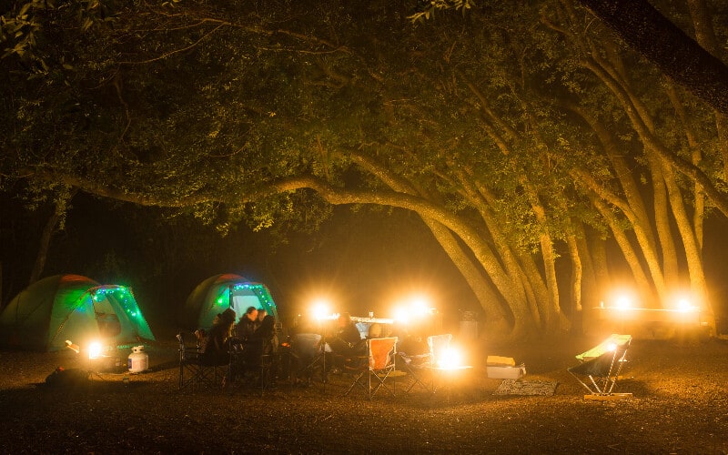 A cluster of camping lanterns illuminating a campsite full of a group of people and two tents.