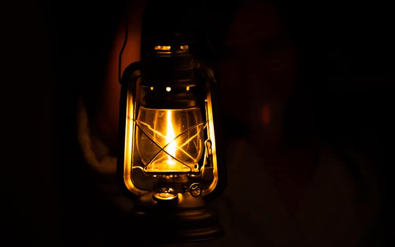 A person holding a fuel lantern in the dark.