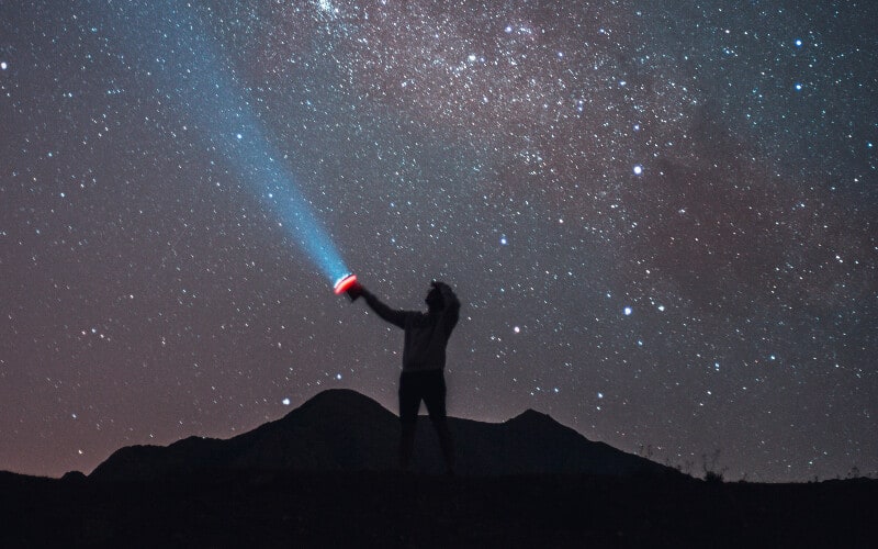 Silhouette of a person holding a flashlight on top of a hill.