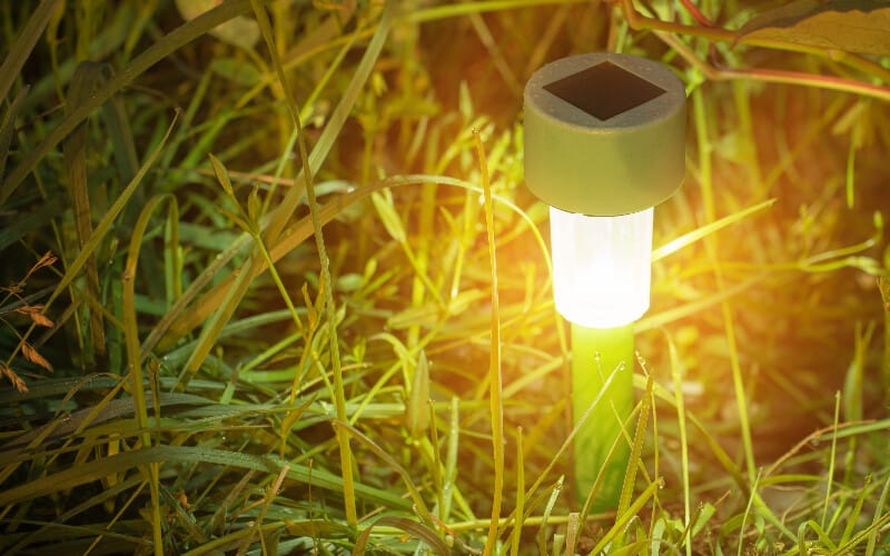 A solar-powered light staked into the ground surrounded by grass.