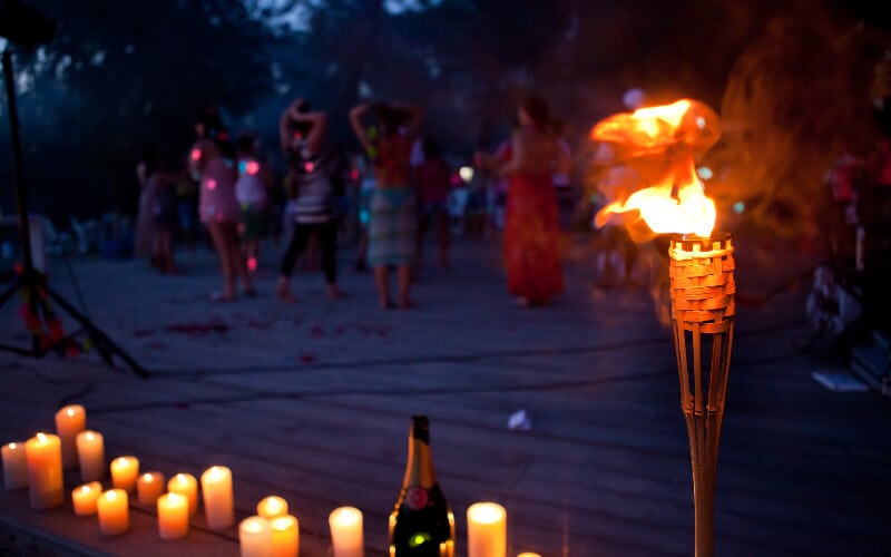 A tiki torch and candles used as camping lighting on a beach with a group of people in the background.