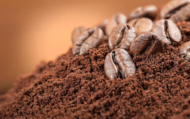 Coffee beans laying on top of coffee grounds.