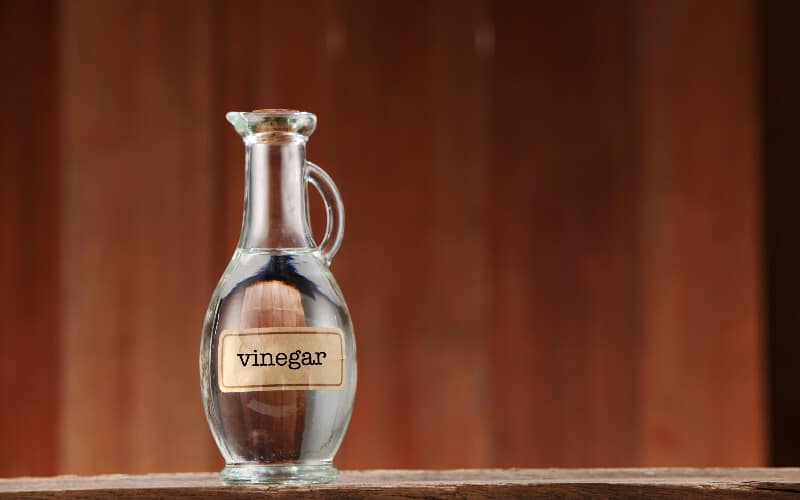A bottle of white vinegar in a glass bottle against a wood background.
