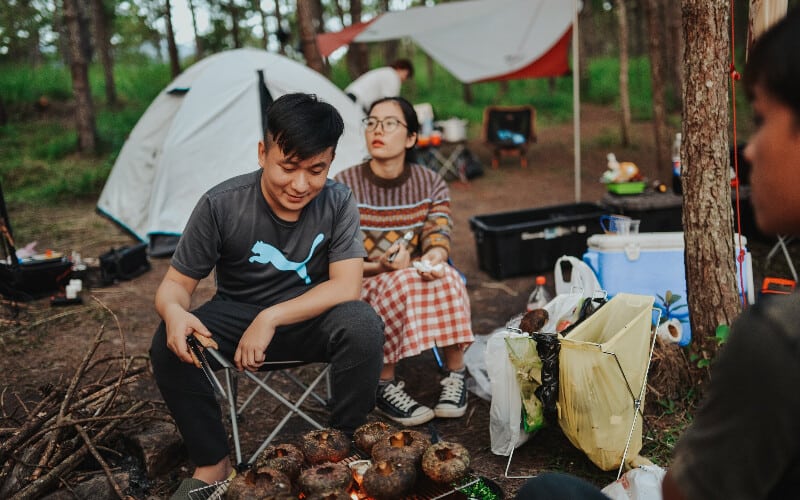 A group of people gathered around a campfire grilling food on a camping trip.