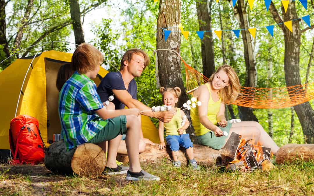 A man and his wife camping with their kids and roasting marshmallows near their tent.