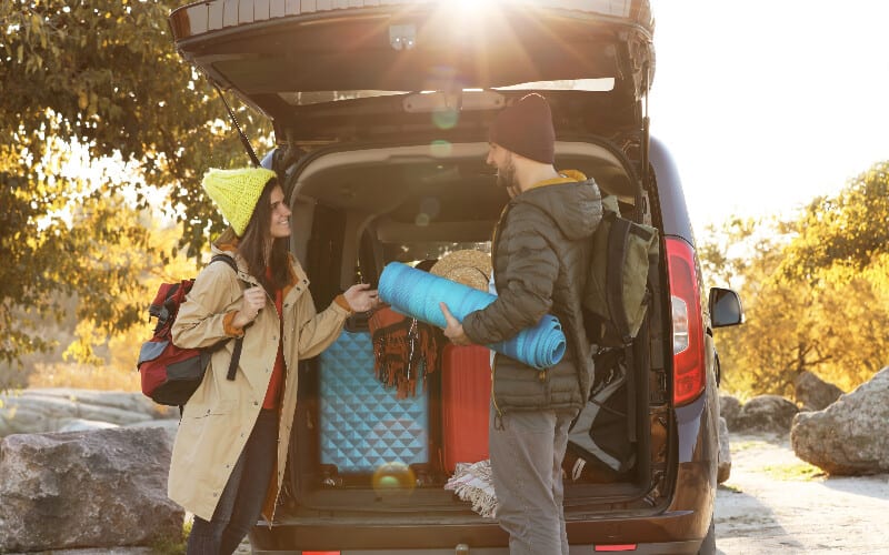 A young couple loading their hatchback while packing for their camping trip.