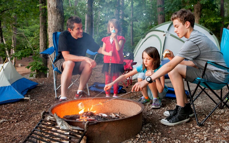 A father roasting marshmallows with his children around a campfire.