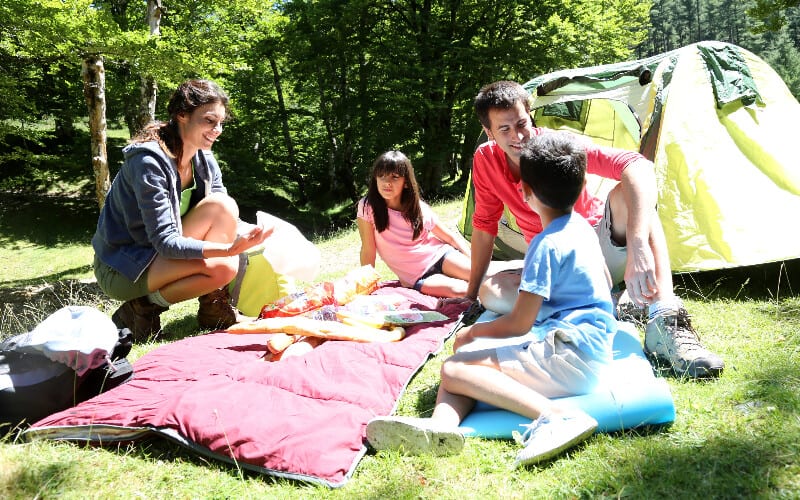 Parents and their children sitting down in front of their tent, enjoying their camping trip.