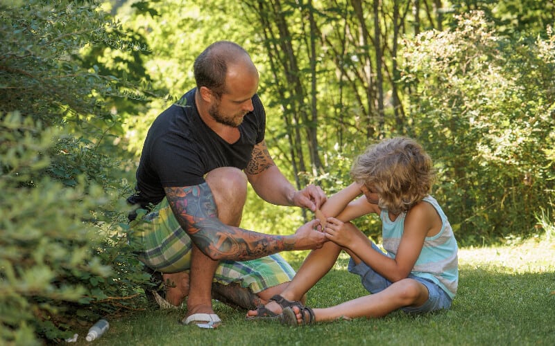 A father putting a bandage on his child's scraped elbow.