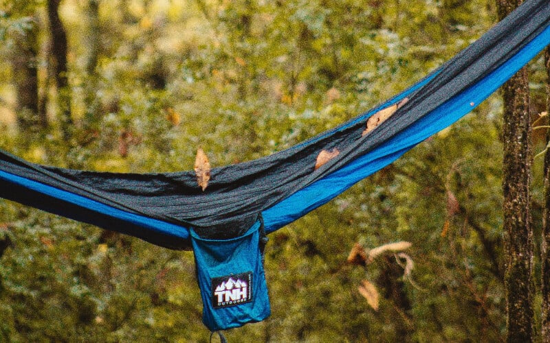A close-up picture of leaves falling on an empty nylon hammock.