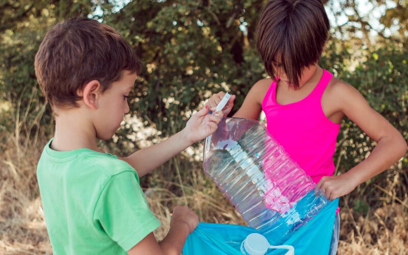 Two boys cleaning a water bottle from their campsite before leaving.