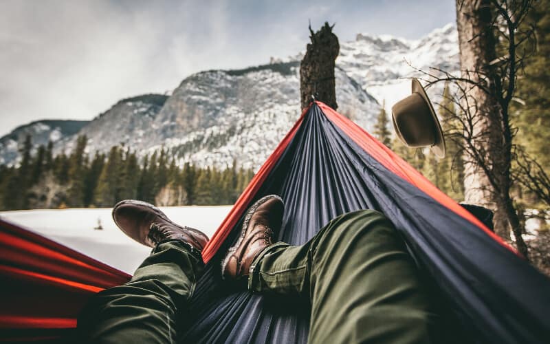 A person's legs pointing diagonally across their hammock with mountains and trees in the background.