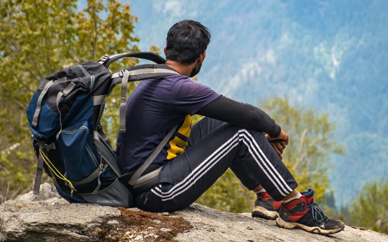 A man wearing hiking clothing with a backpack looking out over a valley.