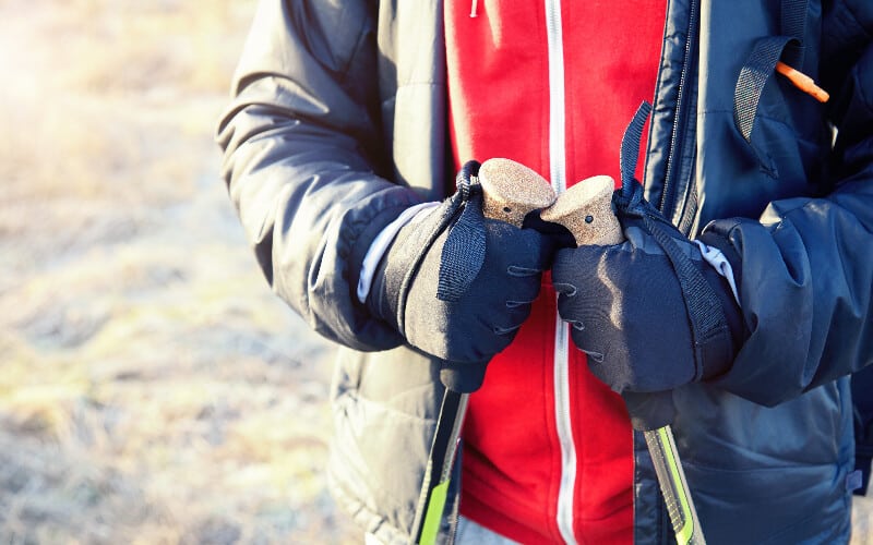 Close up of a man wearing hiking gloves holding trekking poles.
