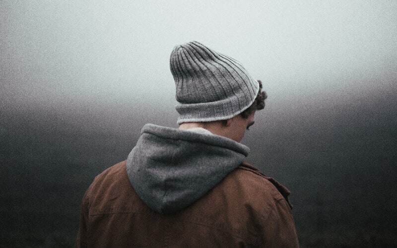 Picture from behind of a man in a hat to keep his head warm on a dark, foggy day.
