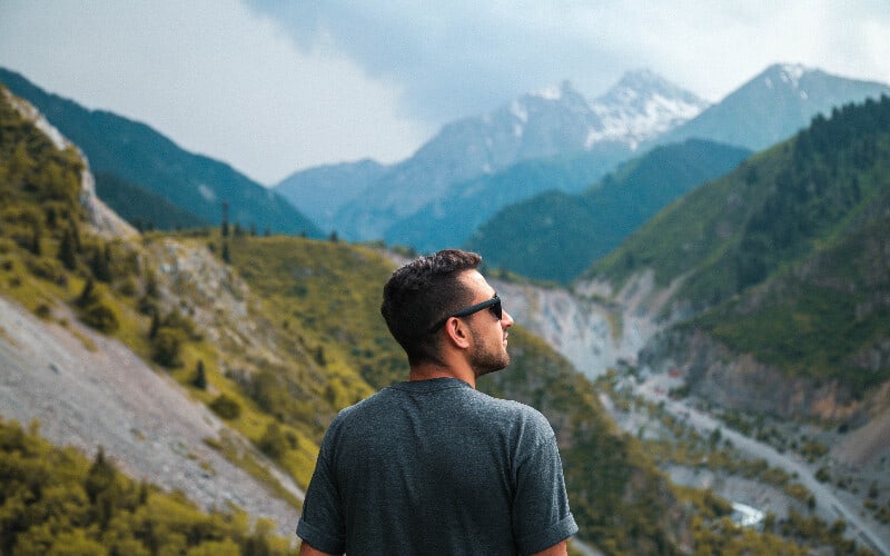 A man wearing sunglasses looking out over a valley during a hike.