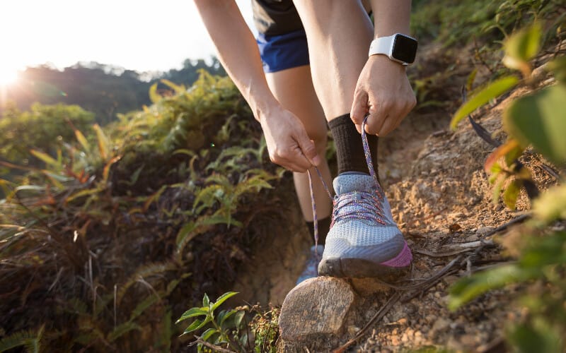 Close up of a woman tying her trail running shoes on a rocky path.