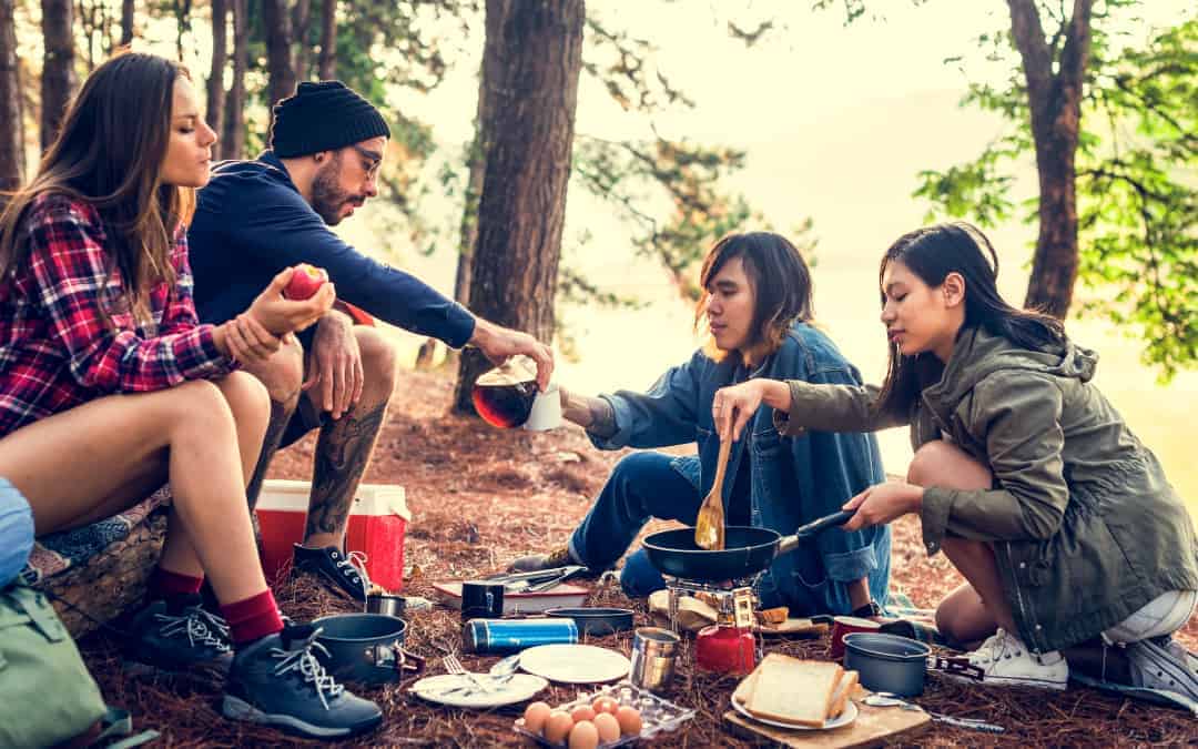 A group of friends cooking a meal in the woods on one of the best camping stoves of 2023.