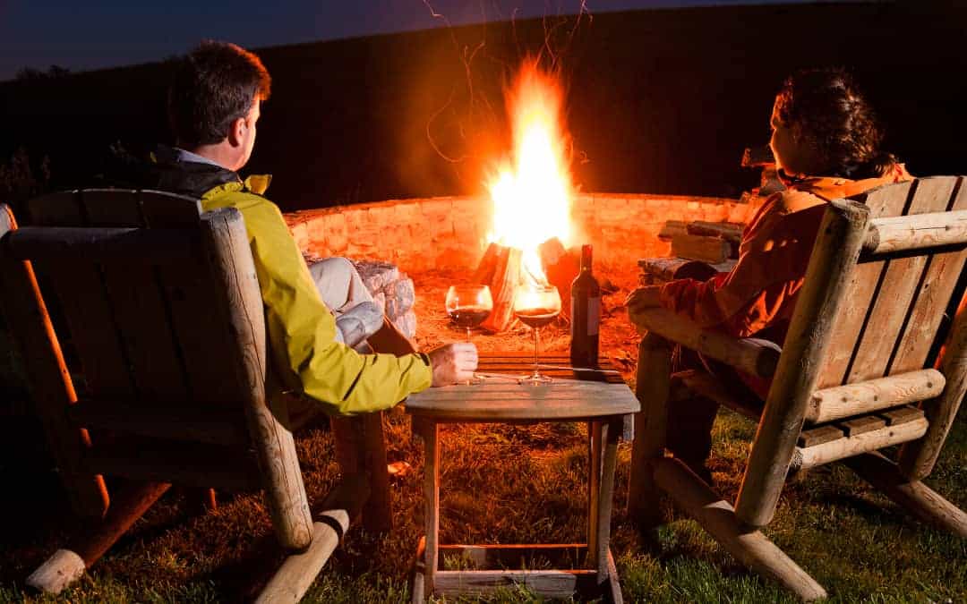 A couple enjoying the ambiance of a romantic camping trip with wine by the fire.
